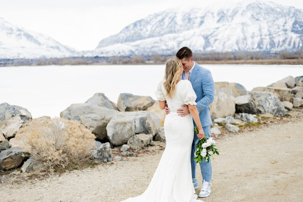 Groom holding bride's waste and touching foreheads with mountains in the background