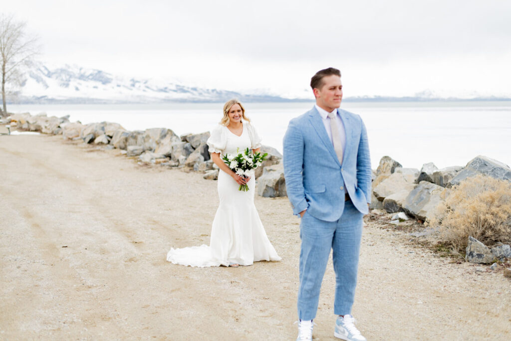 Groom standing with his hands in his pockets while bride stands in the background