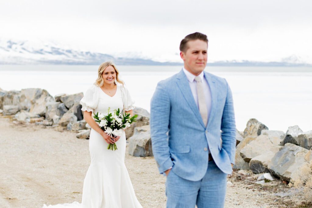 Groom standing with his hands in his pockets while bride stands in the background