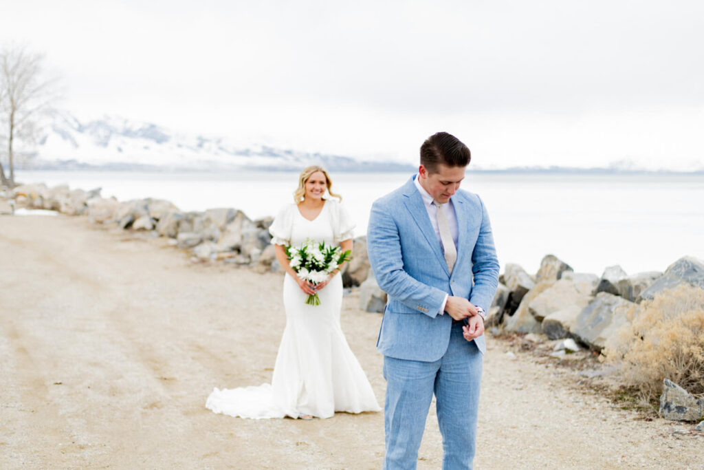 Groom adjusting shirtsleeves while bride stands in the background