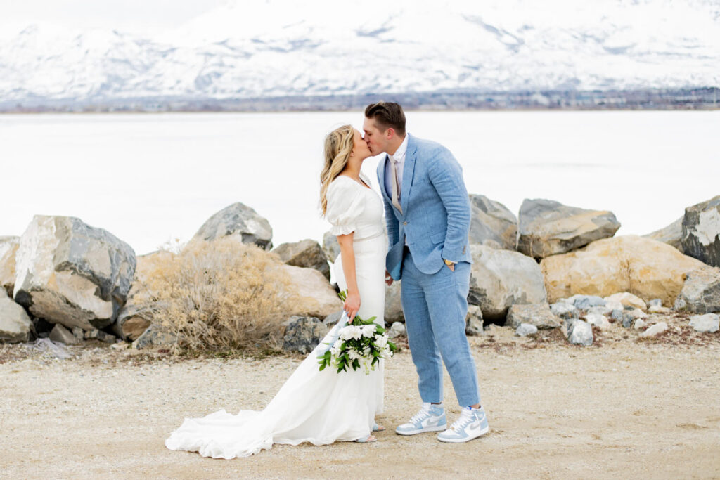 bride and groom kissing with mountains and a lake in the background