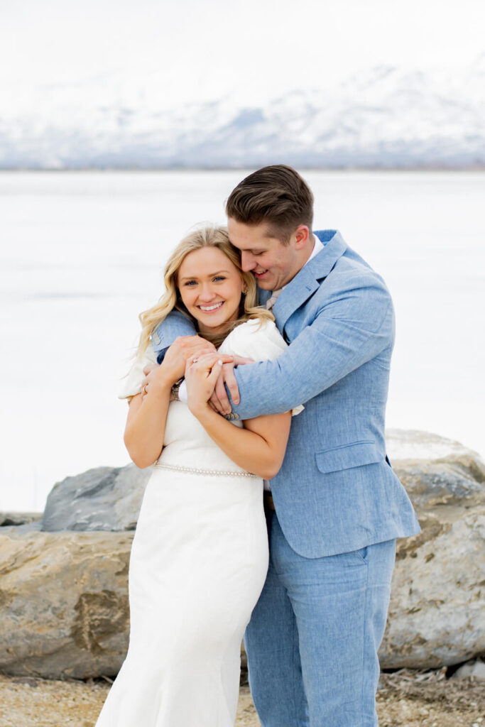 bride hugged from behind by groom with mountain and lake behind them