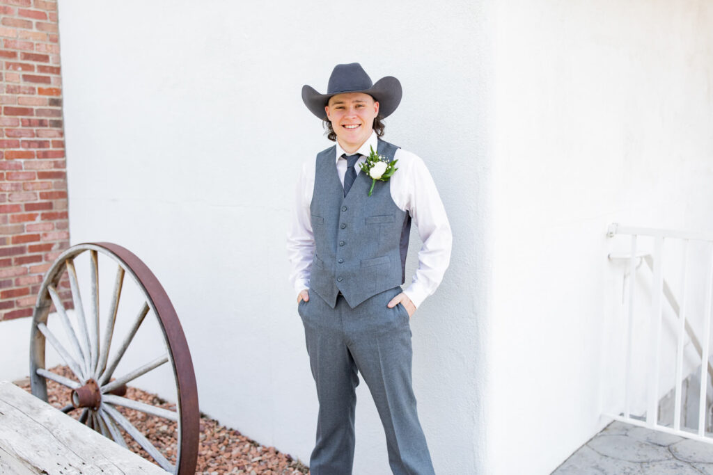 Groom standing against a wall with a wagon wheel in the foreground