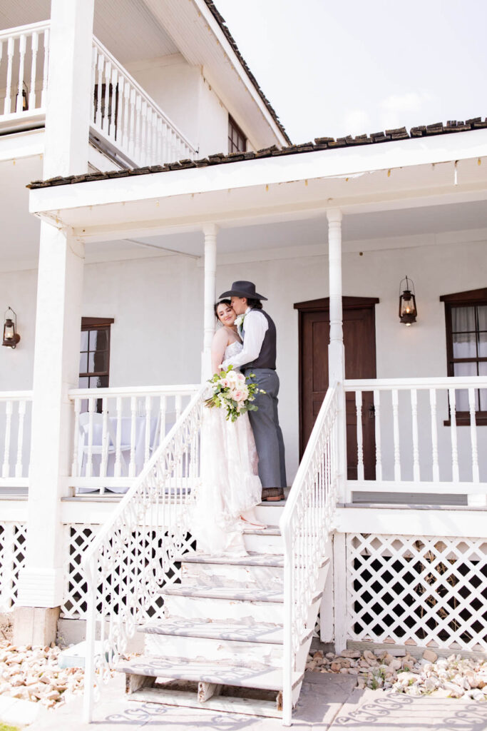 Bride and groom standing against a pillar on a porch and kissing