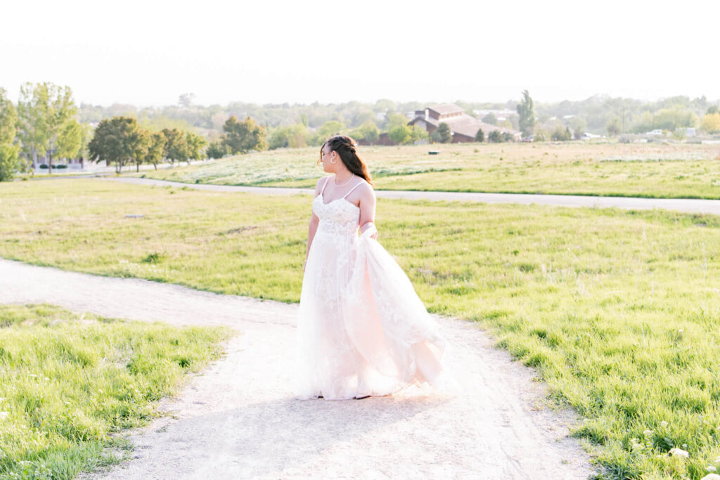 Bride swishing her dress along a dirt road through a field