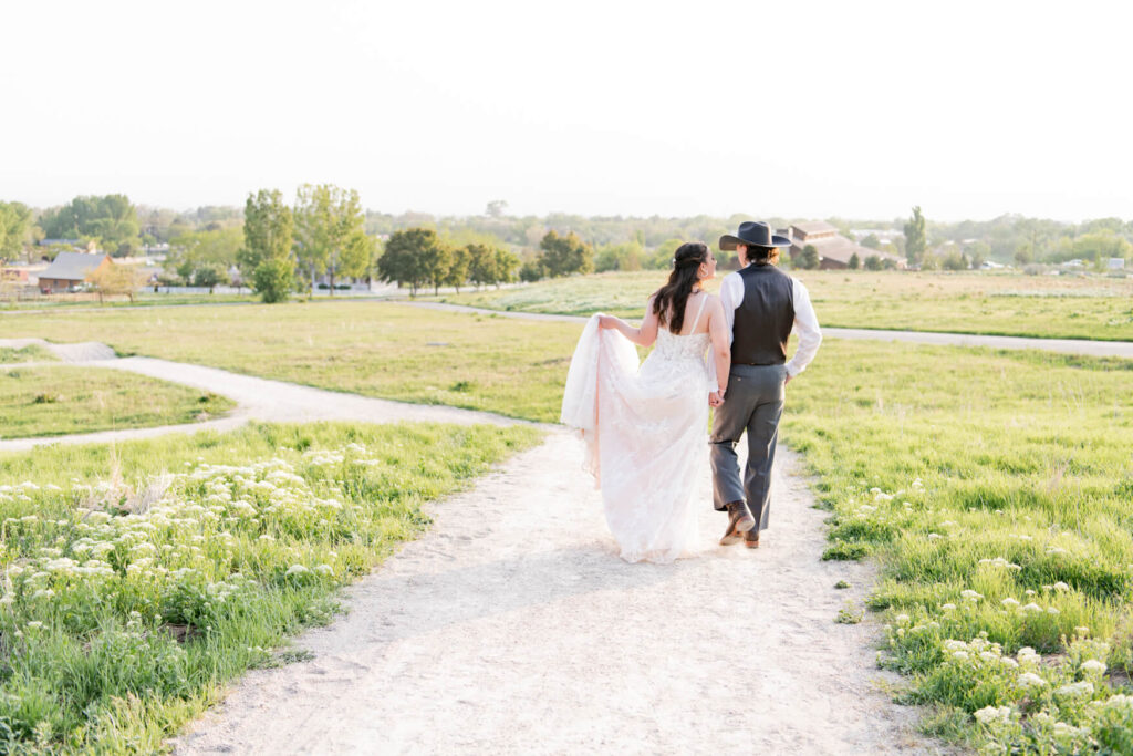 Bride and groom walking away on a dirt path in a field