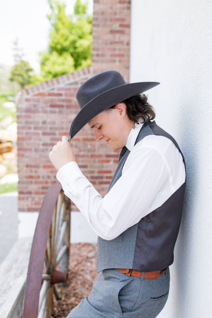 Groom tipping his hat and leaning against a wall