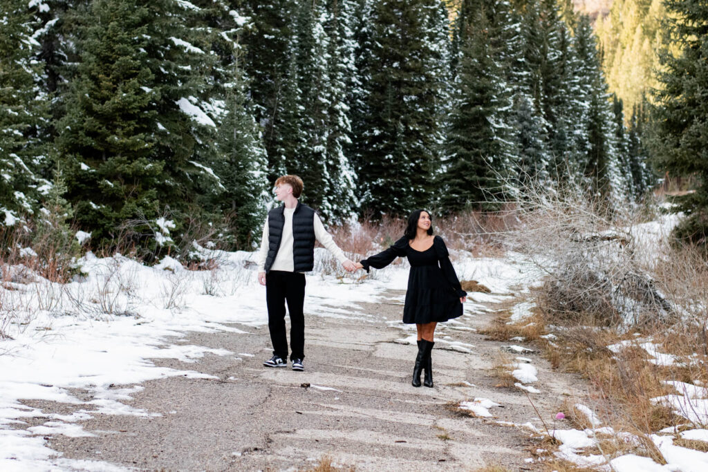 Wide angle shor of a snowy meadow and a man and woman holding hands and looking opposite directions.