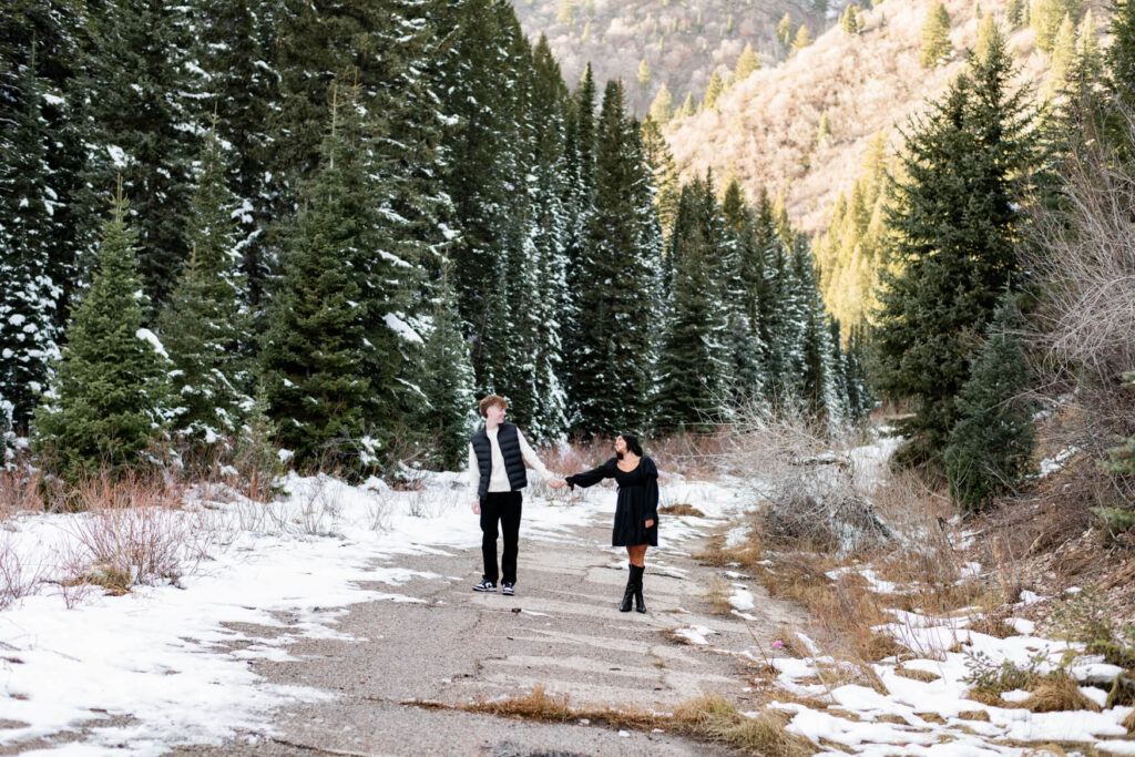 Wide angle shor of a snowy meadow and a man and woman holding hands and smiling at each other