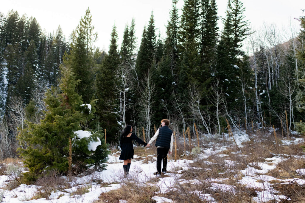 Man and woman holding hands and walking towards some trees.