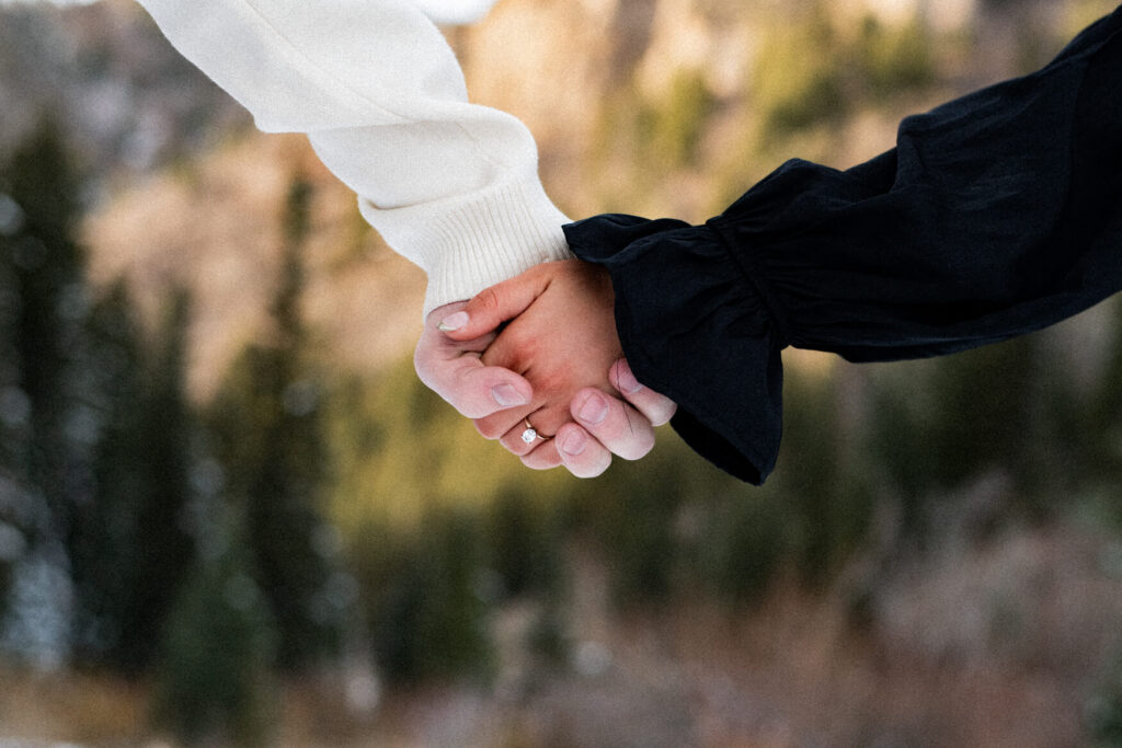 Two people holding hands with a close up of an engagement ring.