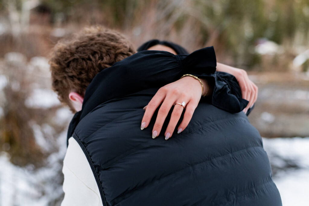 Woman hugging a man with a close up of an engagement ring.