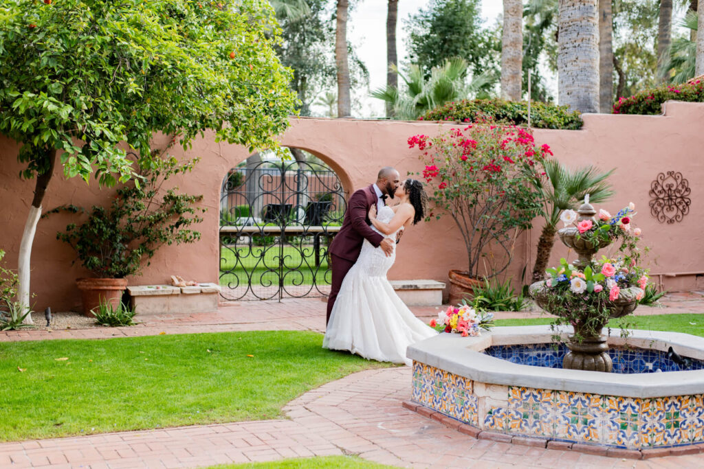 Groom dipping and kissing bride in a courtyard with a fountain and a gate