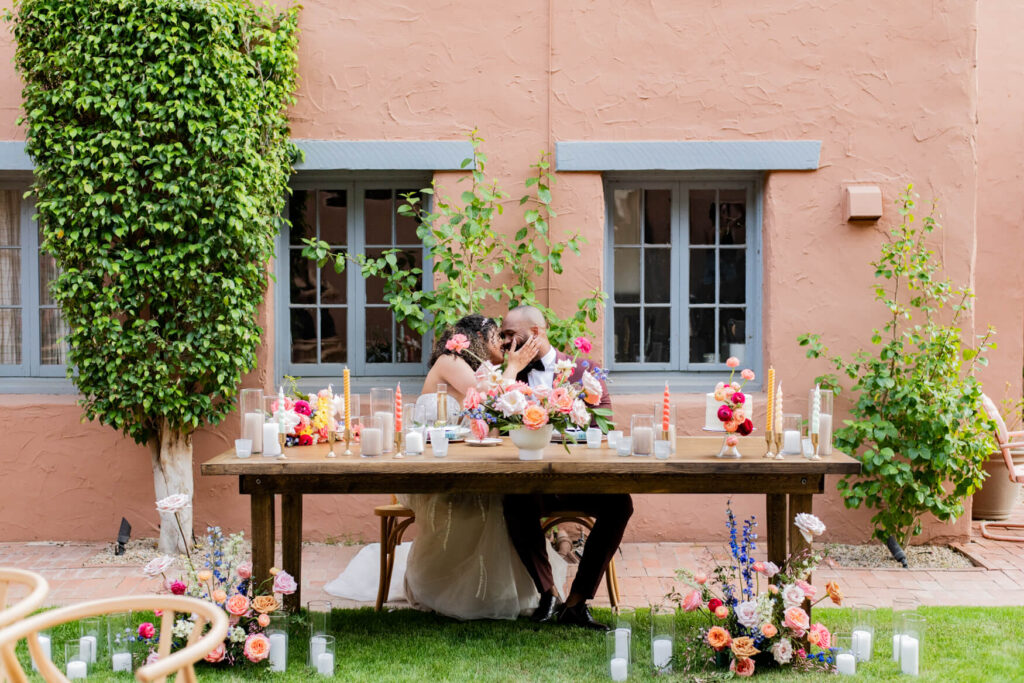 Bride and groom kissing while sitting at their table.