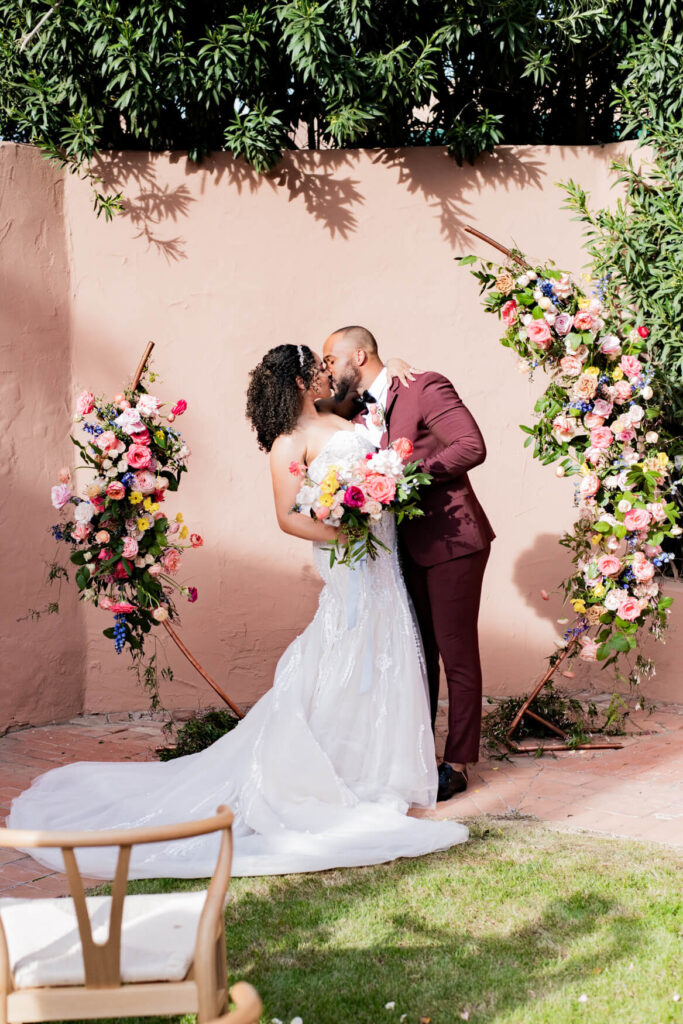 Bride and groom's first kiss in front of a flower arch.