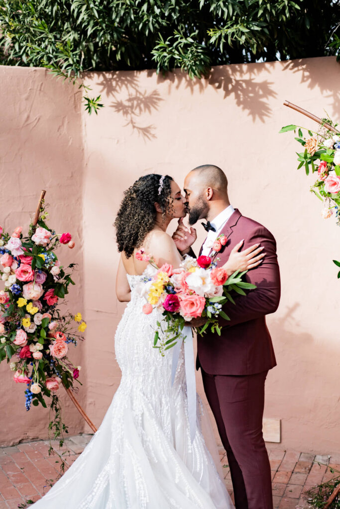 Bride and groom's first kiss in front of a flower arch.