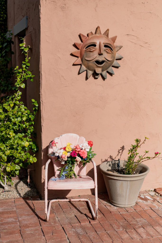 The bride's bouquet on a chair in front of a stucco wall with a bronze sun decal.