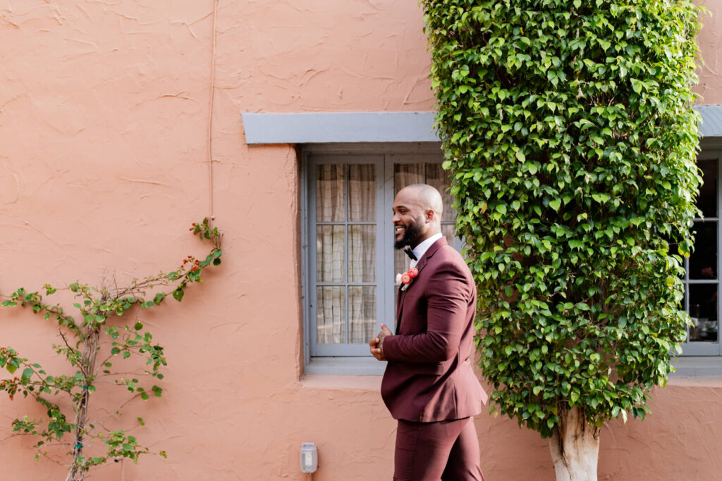 Groom walking in front of a house window while buttoning his jacket.