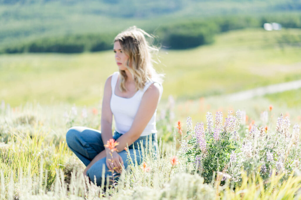Girl sitting down and looking out into the distance, but the focus is on the flowers in front of her