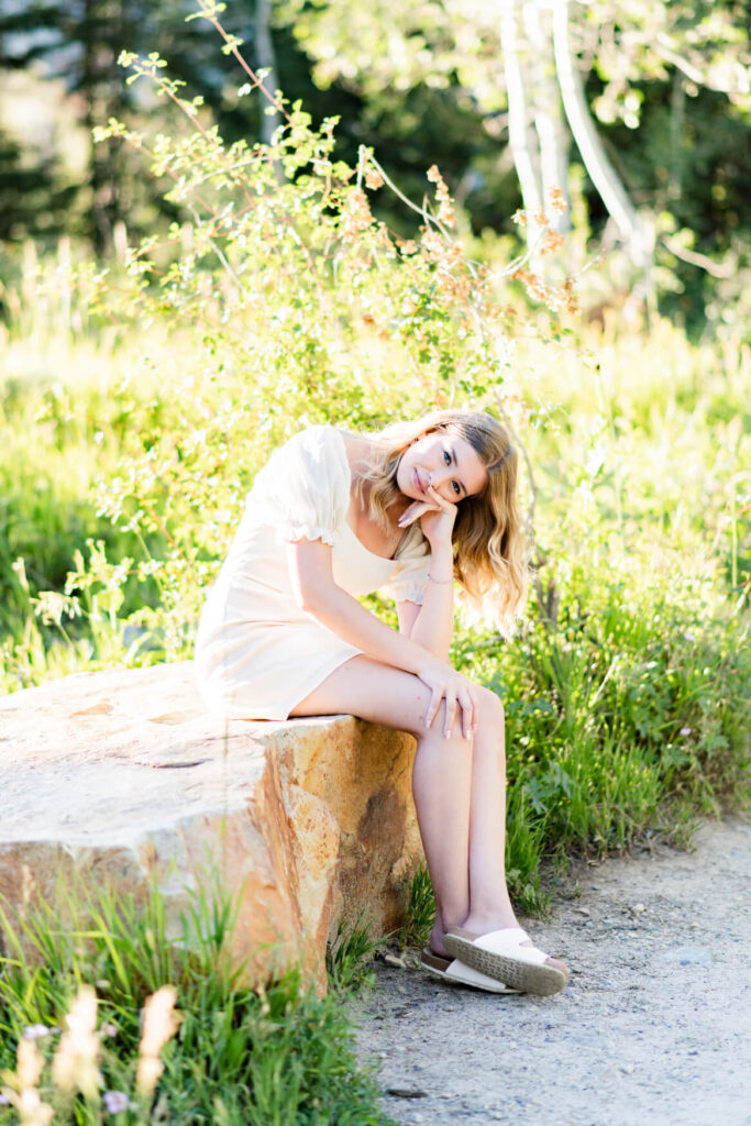 Girl sitting on a rock and leaning over to rest her face on her hand and her elbow on her leg