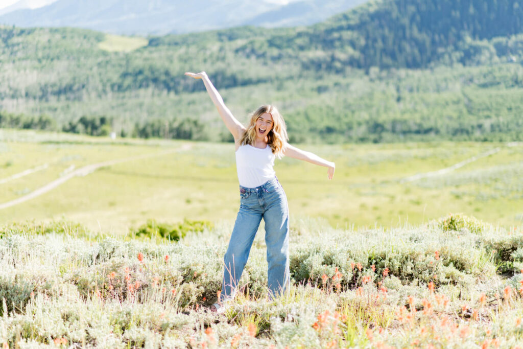 Girl in front of a large meadow with both hands in the air cheering