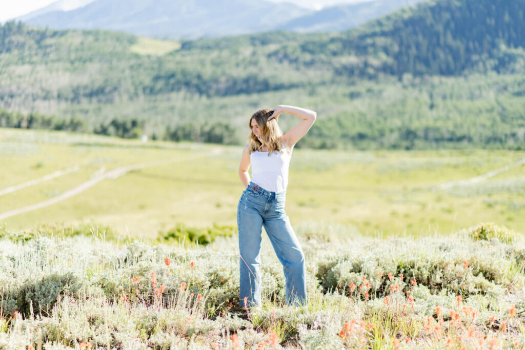 Girl in front of a meadow with one hand on a popped hip and one hand on her head