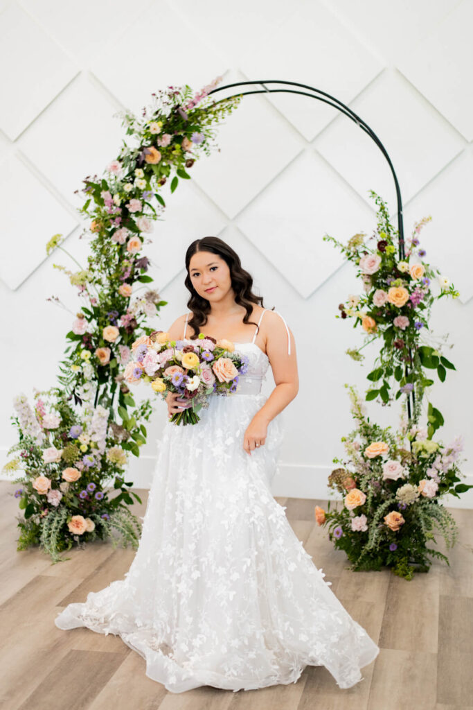 Bride swishing her dress in front of a floral arch