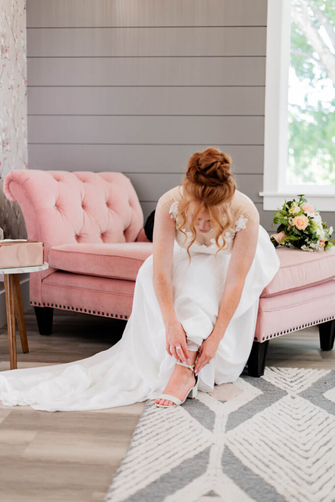 Bride sitting on a pink couch putting on her shoes