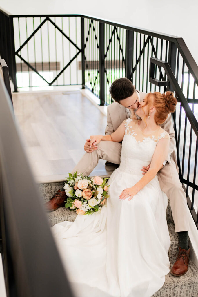 Bride and groom sitting and kissing on some stairs.