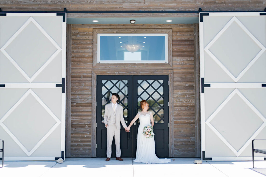 Bride and groom standing in front of the entrance to a building and holding hands