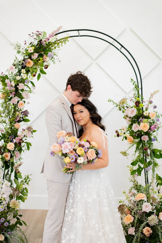 Bride and groom standing together in front of a floral arch