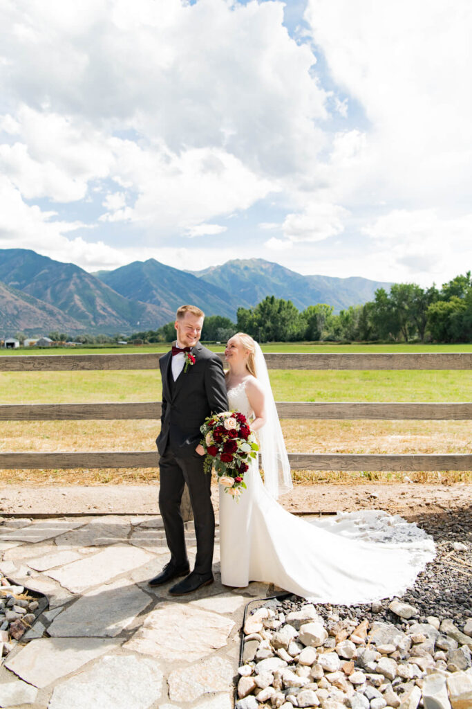 Bride and groom standing together against a fence with a field and mountains in the background