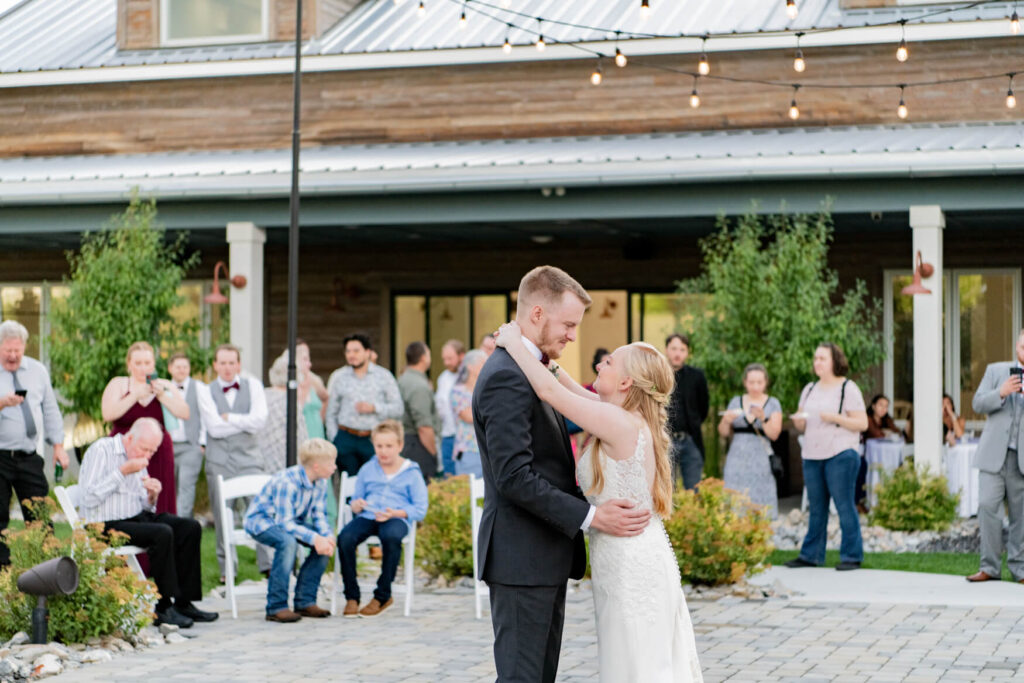 Bride and groom dancing outside on the patio with all of their guests in the background