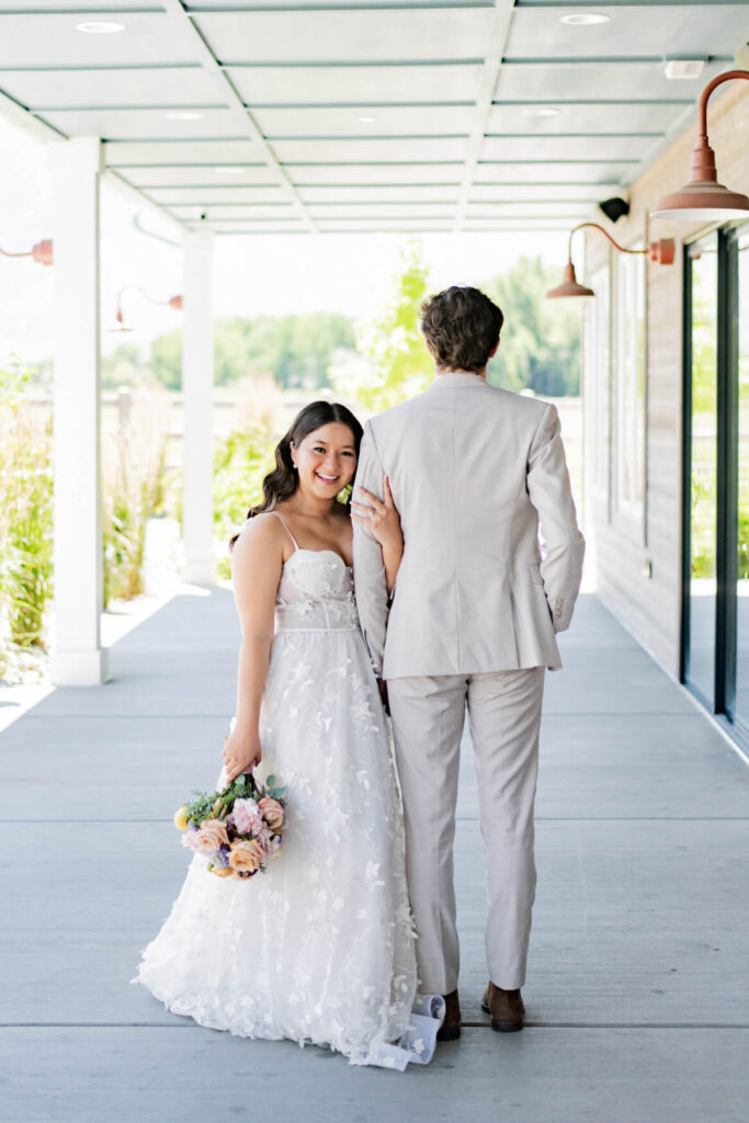 Bride holding grooms arm and smiling at the camera on a patio
