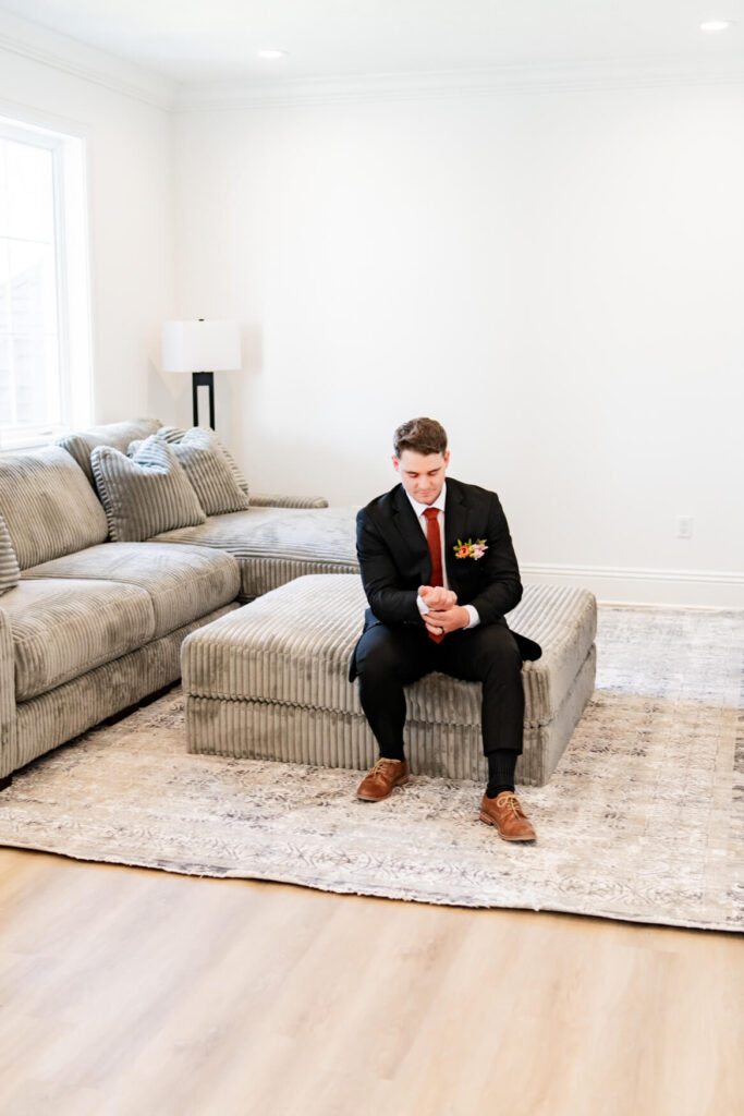 Groom sitting on a couch and fixing his shirt and jacket