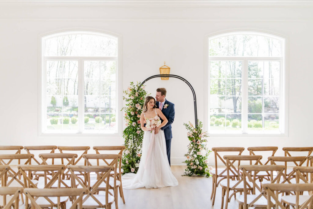 Wedding couple standing next to the ceremony arch and hugging from behind