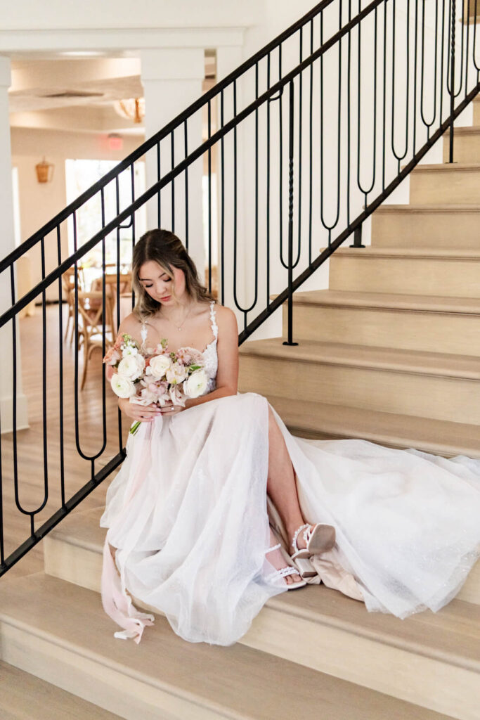 Bride holding flowers and sitting on a staircase looking at her flowers